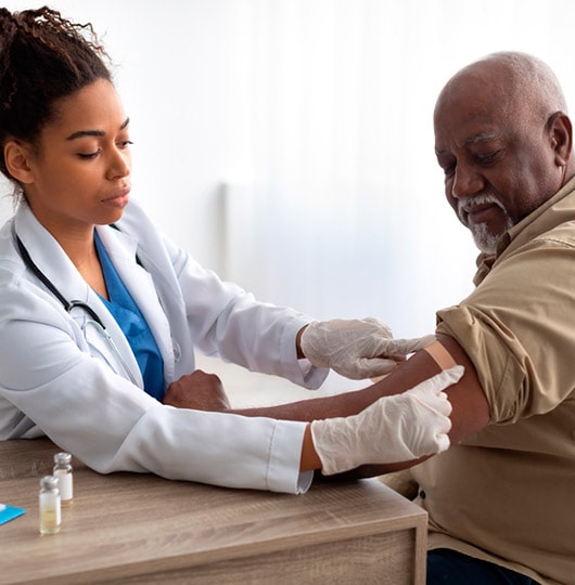 Female doctor placing a bandaid on a male patient’s arm after a vaccination.